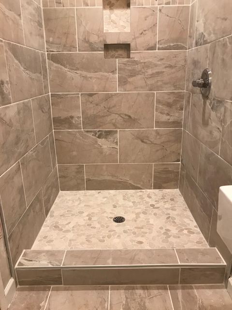 Wide view of tiled shower with pebble floor and drain