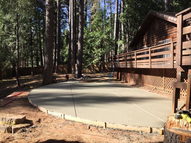 Wide view of poured concrete patio slab beside a cabin deck