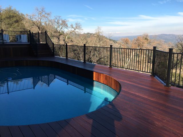 Curved wood deck with metal railing wrapping around a pool, hillside view