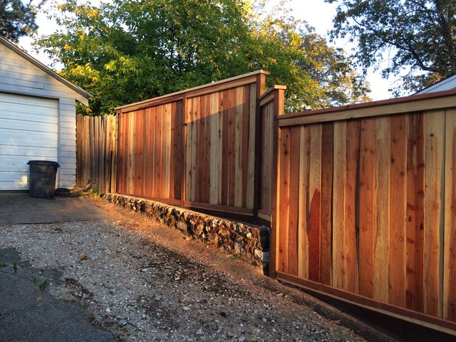 Cedar fence and gate with a stacked stone base along a driveway