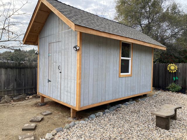 Completed backyard shed with shingled roof and window trim